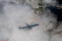 A colorful halo forms around the shadow of a passenger jet on final approach.